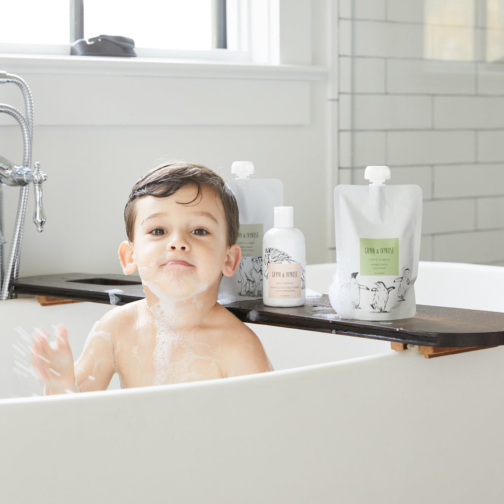 A little boy in the bathtub playing with the set of bath products behind him
